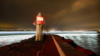 Lighthouse illuminating the night with light trails from a passing ship © Dimitar