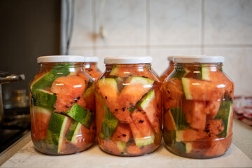 Glass jars of pickled watermelons, rolled up for the winter, stand in the kitchen