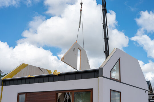 Crane lifting prefabricated wall panel onto modern modular house under construction.