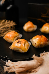 Close-up Indonesian banana–chocolate bolen pastries in paper cups on a dark board; golden flaky puff with sprinkles—ideal for bakery menus, packaging mockups, and social media food ads.