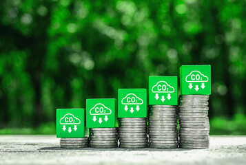 CO2 reduction icon on stack of rising coins with green nature background. Green business concept,...