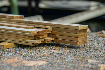 Neatly stacked timber beams beside shoreline.