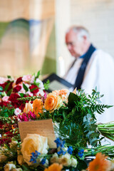 Flower arrangements in foreground of priest.