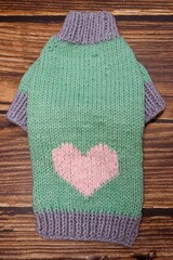 Close knitted mint dog sweater with pink heart on wooden background . warm pet clothes . handmade