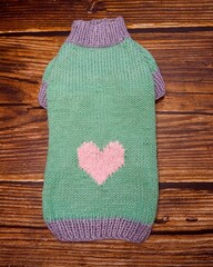 top view of knitted mint dog sweater with pink heart on wooden background . warm pet clothes . handmade