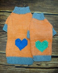 top view of knitted orange dog sweater with blue and mint heart and gray elastic of different sizes . warm clothes for pets . cozy