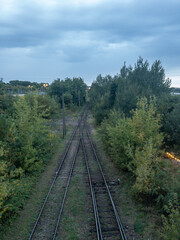 Obraz premium Railway tracks through green forest beside river at dusk, elevated view of transport infrastructure and travel logistics landscape
