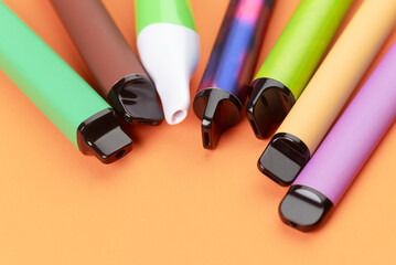 Colorful disposable vape pens on orange background, modern electronic smoking devices closeup.