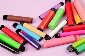 Scattered colorful disposable vapes on pink background, assorted modern electronic cigarettes.