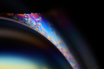 Bright multicoloured liquid surface on black background, interference pattern, one colourful curved line