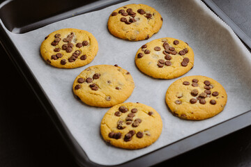 Freshly baked chocolate chip cookies on a baking tray with parchment paper