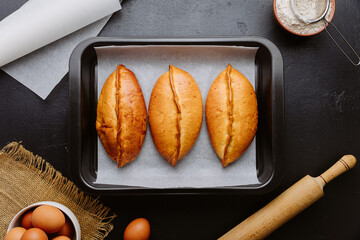 Golden homemade pies in baking tray, rustic kitchen scene with rolling pin and eggs