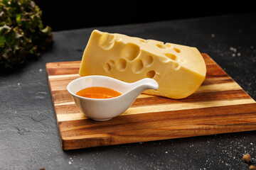 Slice of classic Swiss cheese with holes on cutting board, served with honey and berries