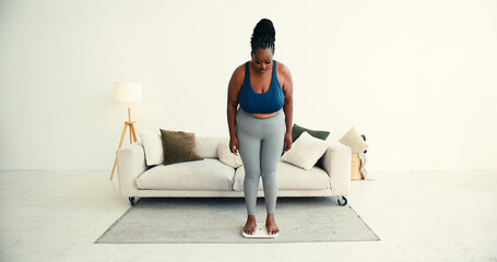 Overweight black woman in sportswear uses smart scale near sofa