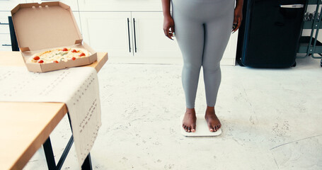 Overweight black woman checks weight on smart scale in kitchen