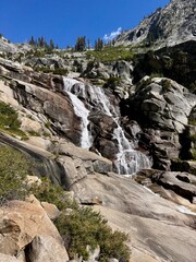 Majestic mountain waterfall cascading down granite cliffs surrounded by rugged alpine scenery and clear blue summer skies.
