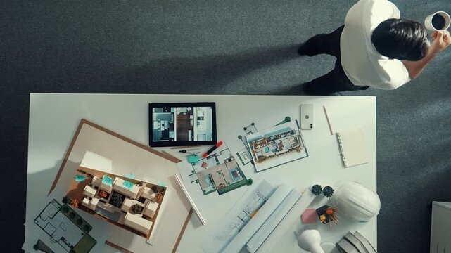 Top view of engineer drink coffee and thinking about house plan at meeting table with equipment and safety helmet scatter around. Aerial view of stressful manager walking and standing. Alimentation.