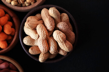 Natural,new harvested peanuts in shell, designed in a wooden bowl on a black surface