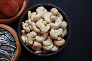 Unroasted, raw cashews were designed in a bamboo bowl on black surface