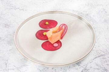 A delicate arrangement features salmon accompanied by vibrant beetroot canvas and pickled onions, presented on a clean white plate. The composition exudes culinary artistry