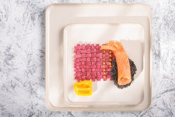 A curated food arrangement features a woven raspberry tile pattern, salmon, black crumble, and yellow pepper on a white plate, reminiscent of a sunset over a sandy beach