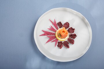 On a white plate, salmon is elegantly arranged like a rose atop a lemon slice, adorned with vibrant...