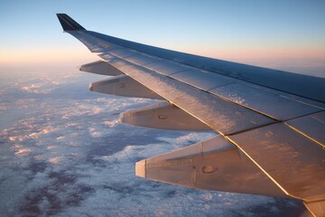 Airplane wing soaring above clouds at sunrise