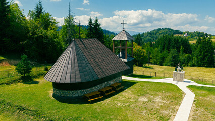 Wooden Orthodox church with cross and memorial monument, located in a mountain village under a clear blue sky