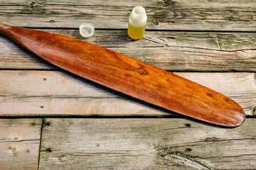 A freshly oiled cherry wood canoe paddle blade and a bottle of tung oil are laid out on a weathered...