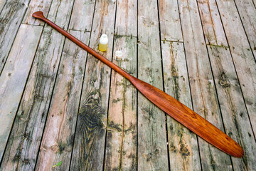 A freshly oiled cherry wood canoe paddle is laid out at an angle with a bottle of tung oil on a...