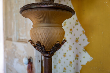 Brass lamp with intricate design on the mantel of an old revolutionary war home with peeling wallpaper and paint in the background