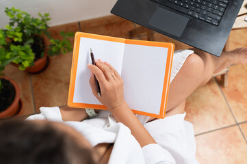 Person Writing in a Notebook with Laptop on a Bright Day