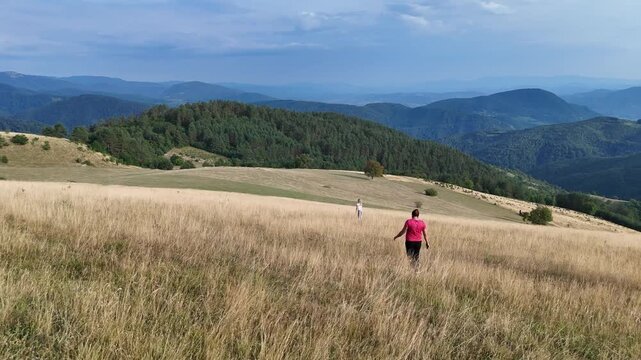 Family hike. Woman and girl enjoying the beautiful view from below the top of the hill. Walking through dry grass. Summer, autumn, outdoor activity.