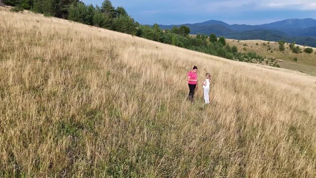 Woman and girl enjoying the beautiful view from below the top of the hill. Walking through dry grass. Summer, autumn, outdoor activity, family.