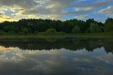 Calm summer evening, dusk after sunset on a forest lake. Harmonious widescreen panoramic side view of the shore, overgrown with trees. Harmony of HDR style.