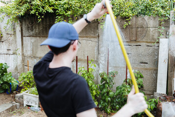 One young guy is watering raspberries with a yellow hose.
