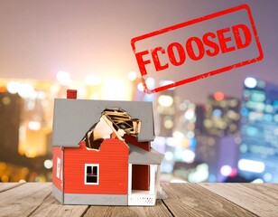 A miniature house with a large hole, a red stamp saying "FCOOSED" over a blurred city at night
