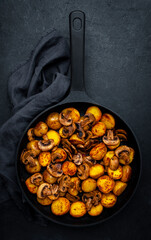 Yummy baked potatoes with mushrooms in frying pan. Black background, top view