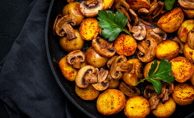 Baked golden potatoes with mushrooms in frying pan. Black background, top view