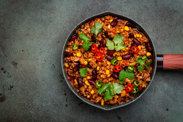 Chili con carne with beef, beans, paprika, corn, cilantro, jalapeno in tomato sauce, in frying pan, rusty green background top view