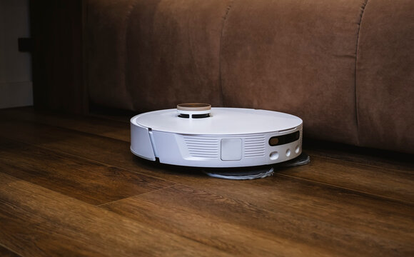 White robot vacuum cleaner mopping floors and vacuuming while cleaning in beautiful modern bedroom