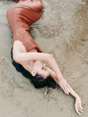 Relaxed woman lying on sandy beach in rust dress with closed eyes, peaceful mood, natural background, summer vibes, beauty and calmness.