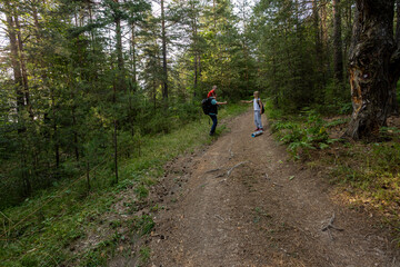Hiking in the forest, a boy with Down syndrome on his father's shoulders and his sister playing. Parents and kids enjoying active outdoor day in forest.