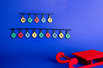 Red sleigh with a garland of colored lights spelling out “Merry Christmas.” On a blue background