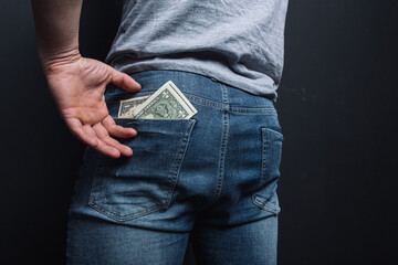 young guy shoves crumpled old paper money. concept: poverty and unemployment, benefits and low wages. financial literacy for students. man's ass in jeans close-up