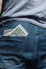 young guy shoves crumpled old paper money. concept: poverty and unemployment, benefits and low wages. financial literacy for students. man's ass in jeans close-up