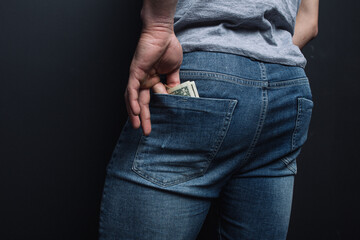 young guy shoves crumpled old paper money. concept: poverty and unemployment, benefits and low wages. financial literacy for students. man's ass in jeans close-up
