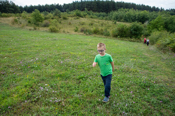 Little boy running in the field. Outdoor family activity, enjoying fresh air and green trees....