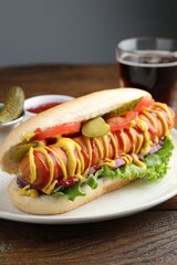 Tasty hot dog served with soda drink on wooden table, closeup