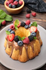 Tasty Bundt cake with berries, chocolate and mint on wooden table, closeup